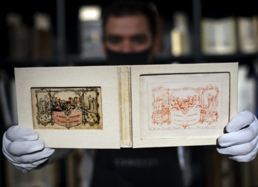 A gallery assistant holds the first printing of the first commercial Christmas greetings card (Victoria Jones/PA)