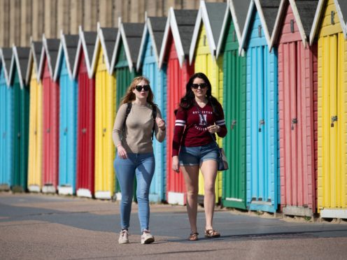 People make their way past beach huts on the sea front on Boscombe beach (Andrew Matthews/PA)