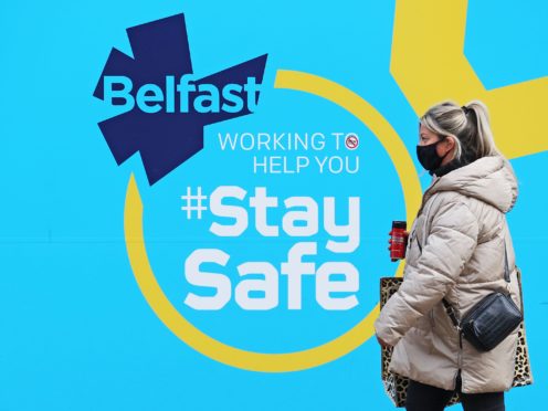 A woman wearing a face mask walks past a public information sign in Belfast as Northern Ireland remains in an extended lockdown to curb the spread of coronavirus and lower infection rates.