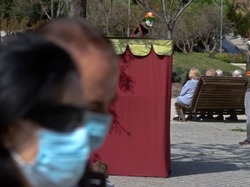 A couple wearing protective masks walk past a puppet show in a park in Madrid, Spain (Paul White/AP)