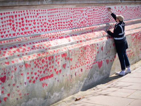 A volunteer adds hearts to the Covid-19 memorial wall in Westminster, central London (Dominic Lipinski/PA)