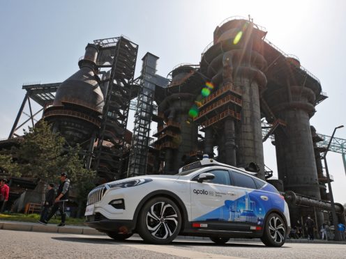 A Baidu Apollo Robotaxi move past a steel plant at the Shougang Park in Beijing, Sunday, May 2, 2021. Chinese tech giant Baidu rolled out its paid driverless taxi service on Sunday, making it the first company that commercialized autonomous driving operations in China. (AP Photo/Andy Wong)