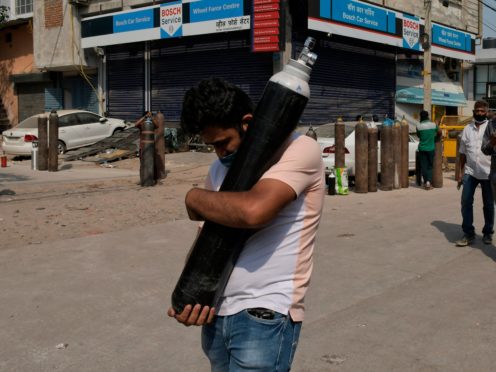 A man walks carrying a refilled cylinder as family members of Covid-19 patients wait in queue to refill their oxygen cylinders at Mayapuri area in New Delhi, India (Ishant Chauhan/AP)