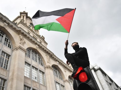 A demonstrator waves a Palestinian flag whilst sat atop a traffic light in London (PA)