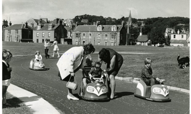 Children driving the electric cars around the race track at Castle Green, Broughty Ferry, while two women help one of the kids into one of the cars. The picture was taken on August 21 1972.