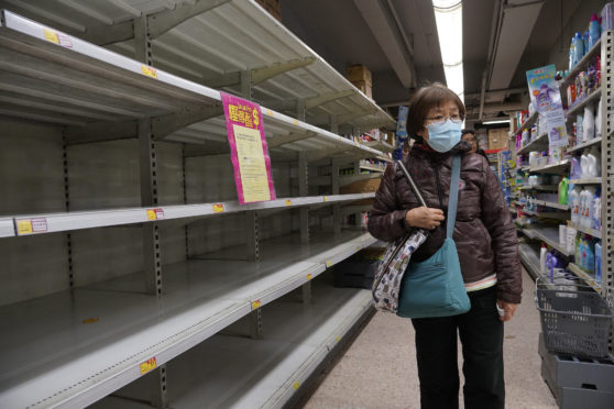 A woman wearing face mask walks past empty shelf of tissue papers at supermarket in Hong Kong.