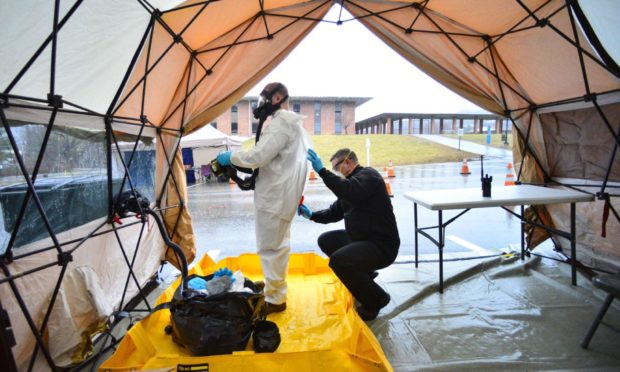 Sgt. First Class Mason Lord, with the Vermont Army National Guard, helps remove a personal protective equipment suit in a decontamination zone at the Covid-19 testing facility in a parking lot in Vermont.