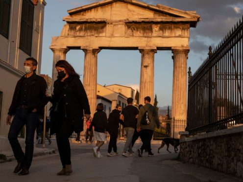 People wearing face masks walk in front of the Gate of the Ancient Roman Agora in the Plaka district of Athens (Petros Giannakouris/AP)