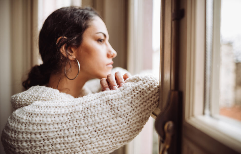 Millennial woman looking out the window feeling lonely