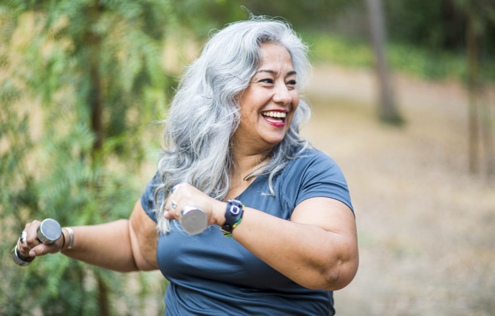 Happy older woman smiling and using weights outdoors