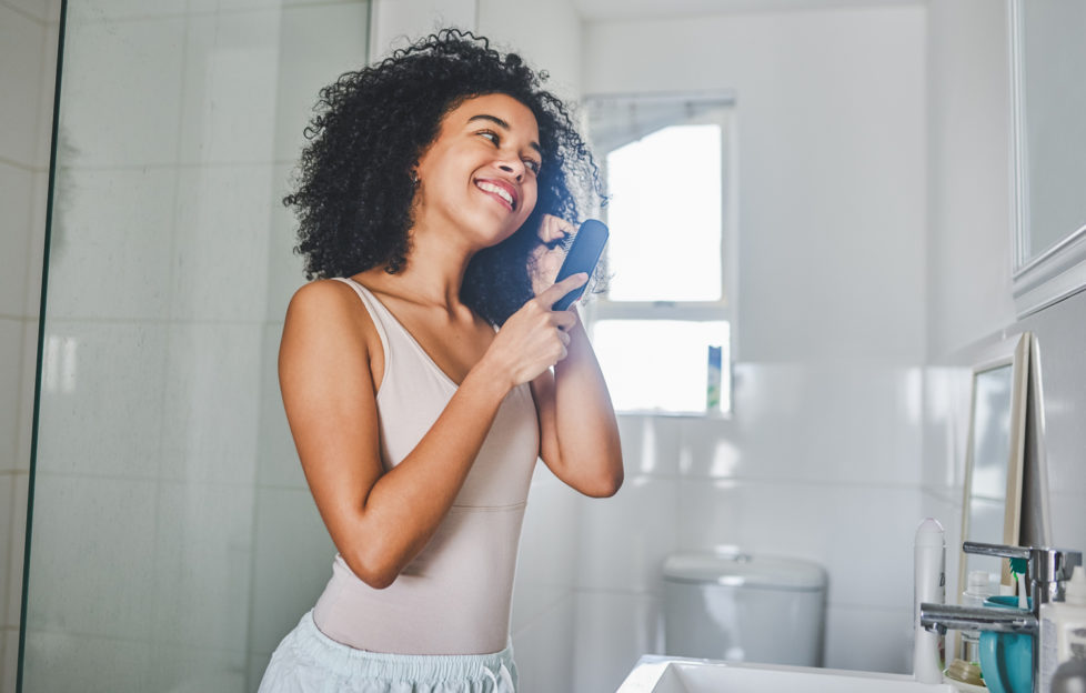 Woman brushing her hair inside her bathroom, after learning not to make these hair mistakes