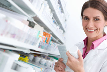 A smiling female pharmacist reading medicine bottle in pharmacy
