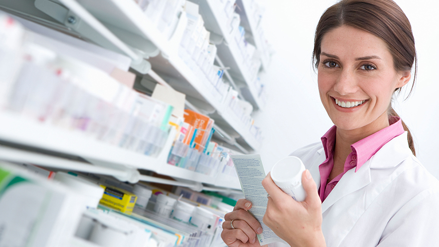 A smiling female pharmacist reading medicine bottle in pharmacy