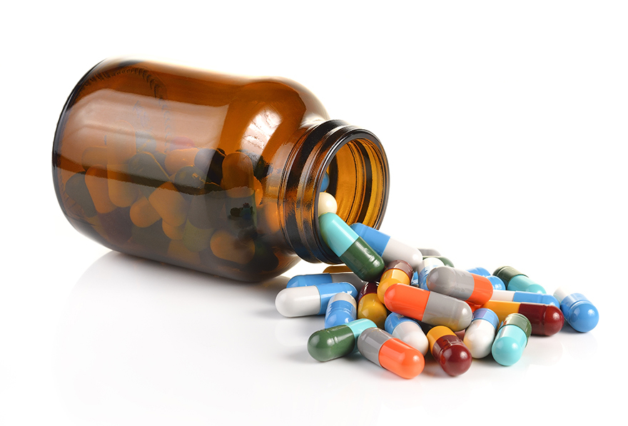 Multi-coloured pill capsules spilling out of a bottle