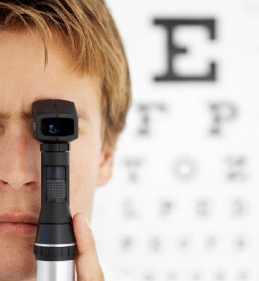 Male optician holding up light, with Snellen chart behind