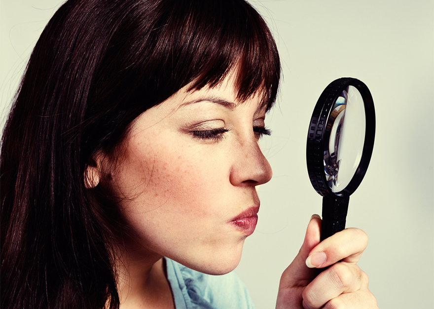 Woman peering through magnifying glass, looking suspicious