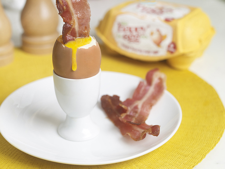 Bacon being dipped in a boiled egg