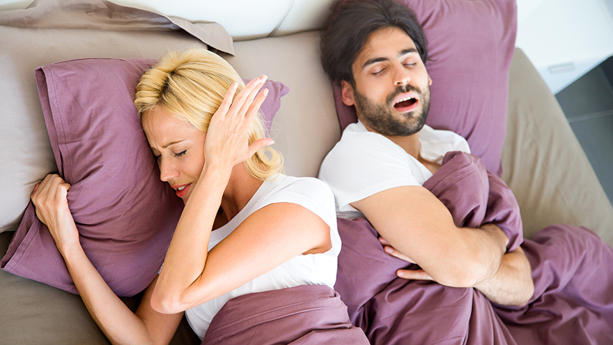Woman covering ears while man snores in sleep.