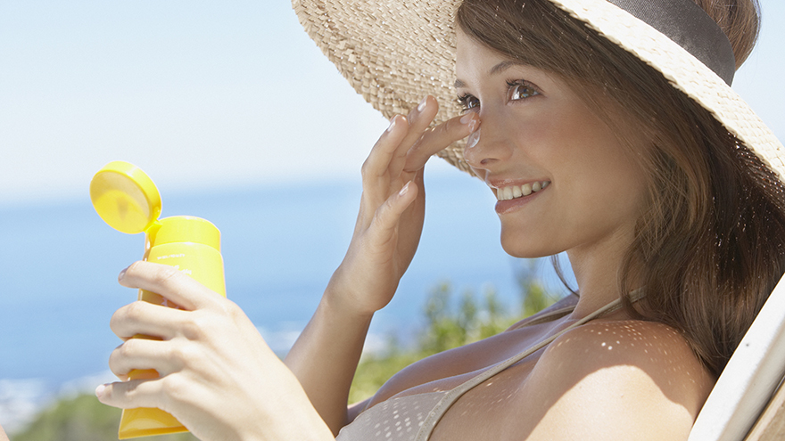 Woman with straw hat applying sun block to face outdoors