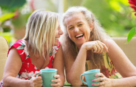 Two middle aged women with mugs of tea, laughing together