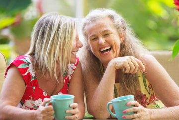 Two middle aged women with mugs of tea, laughing together