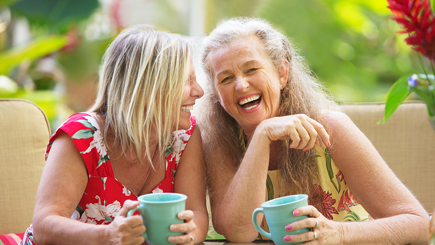 Two middle aged women with mugs of tea, laughing together