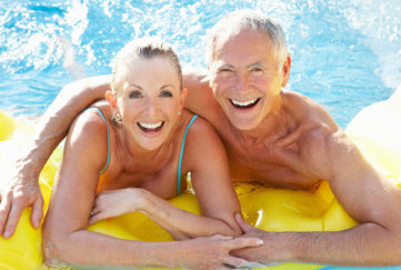 Senior couple having fun in pool outdoors smiling to camera