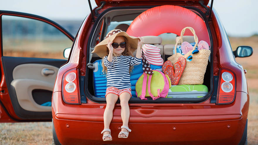 Small girl sitting in open boot of car at seaside