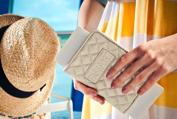 Close up of female hands holding passport and boarding pass with luggage trolley in the background.