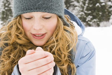 Young woman in woollen hat blowing on her hands in the cold