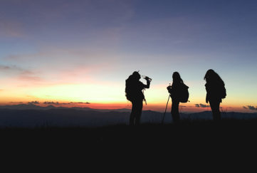 Silhouettes of group hikers people with backpacks enjoying sunset view from top of a mountain.
