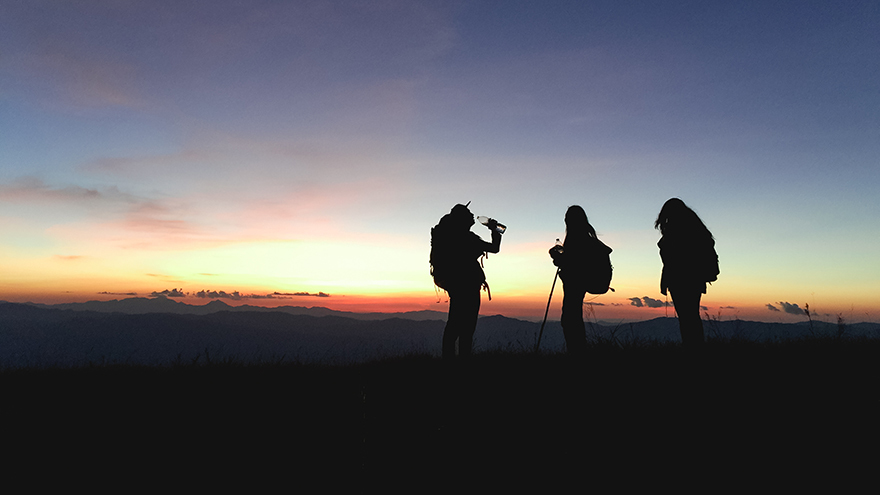 Silhouettes of group hikers people with backpacks enjoying sunset view from top of a mountain.