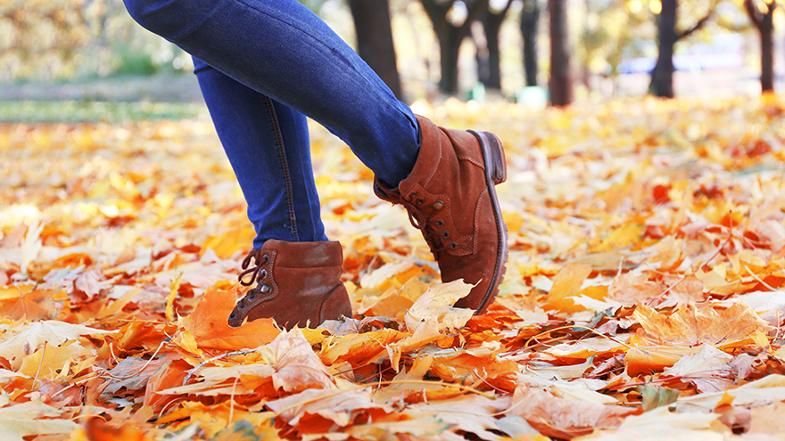 Woman in jeans and boots kicking leaves