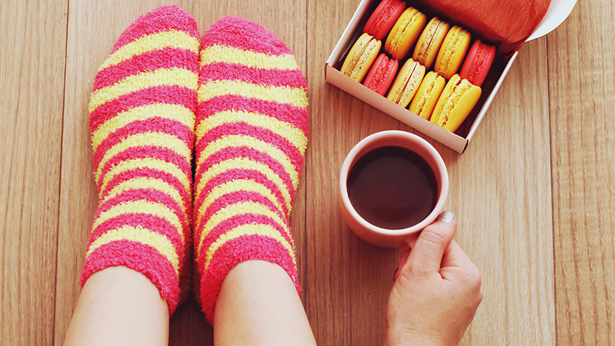 Woman's feet in stripey socks with cup of coffee and macroons