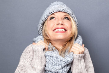 dreaming young blond woman with winter hat and imagination feeling cozy, enjoying a happy season holidays, grey background