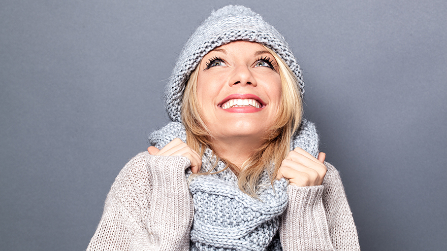dreaming young blond woman with winter hat and imagination feeling cozy, enjoying a happy season holidays, grey background