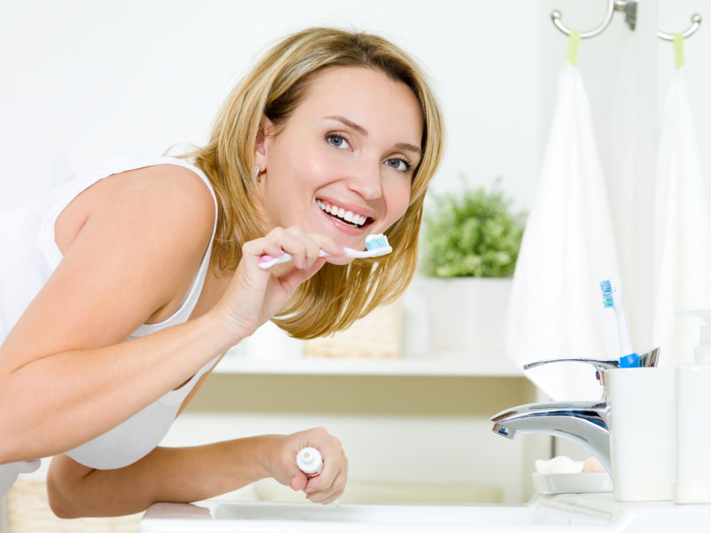 Young happy caucasian woman cleaning teeth with toothbrush in bathroom