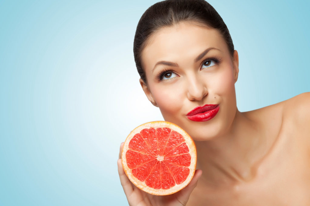 A creative portrait of a beautiful girl holding a fresh ripe grapefruit.