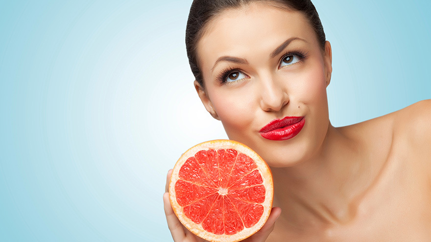 A creative portrait of a beautiful girl holding a fresh ripe grapefruit.