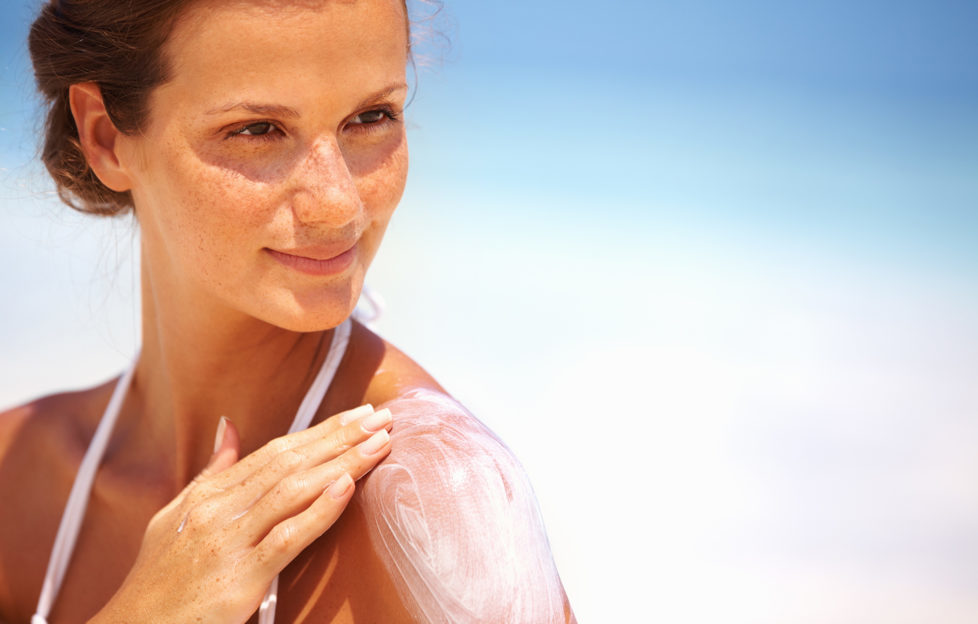 Closeup of lovely young woman applying sunscreen lotion on body