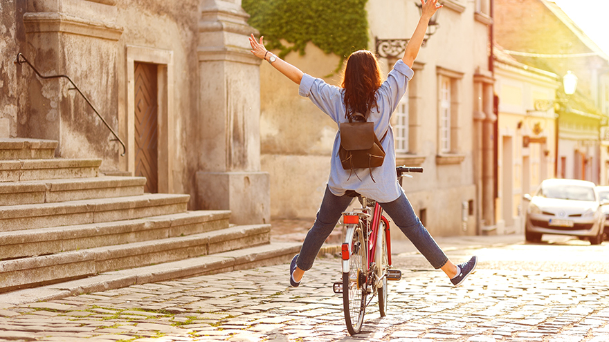 Rear view of young woman riding a bicycle down the street at sunset.