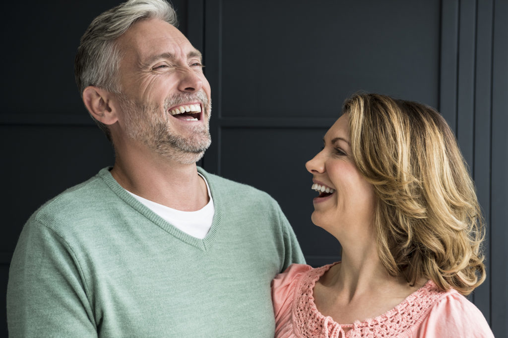 Mature couple smiling and laughing in front of dark blue panelling