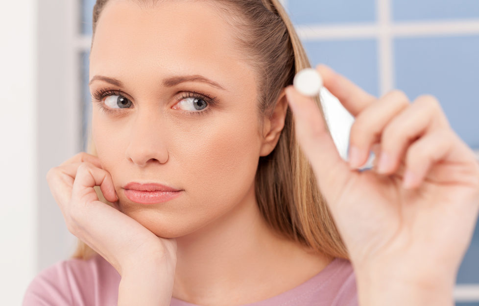 Depressed young woman holding a pill and looking at it