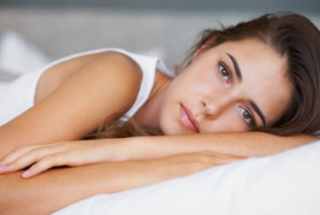 A beautiful young woman looking sad while lying on her bed