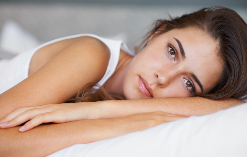 A beautiful young woman looking sad while lying on her bed