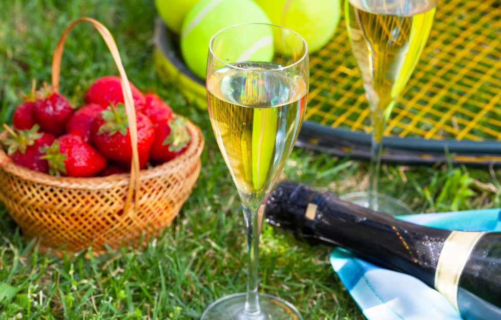 Strawberries, champagne and tennis balls on racket in the grass