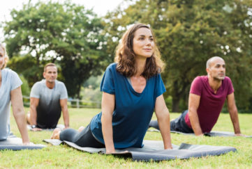 Mature healthy people doing yoga at park. Group of multiethnic people exercising on green grass with yoga mat. Happy men and smiling women in yoga class doing exercise outdoor."r