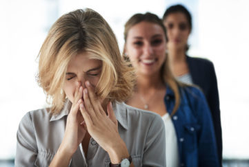 Woman sneezing as women behind her smile