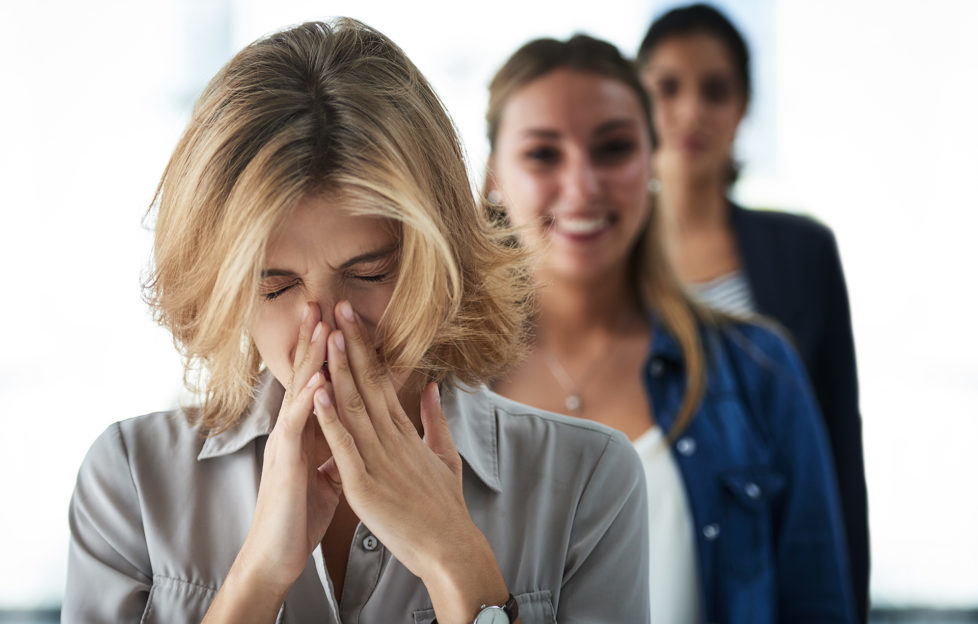 Woman sneezing as women behind her smile