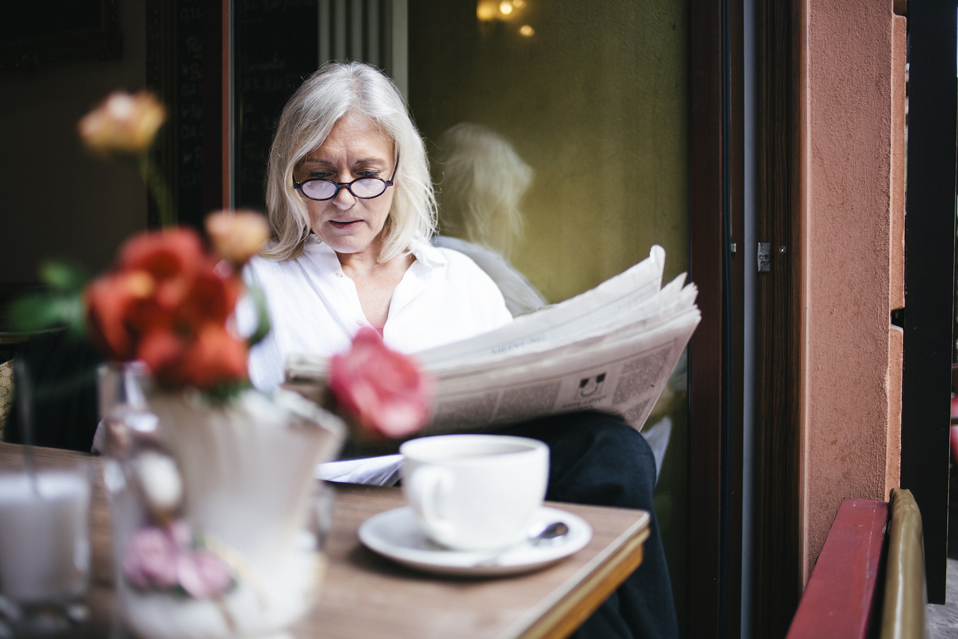 senior woman sits in a Sidewalk Cafe at an open window and reads a newspaper